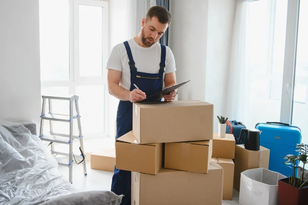 Technicien de débarras en tenue bleue notant l'inventaire sur un clipboard entouré de cartons